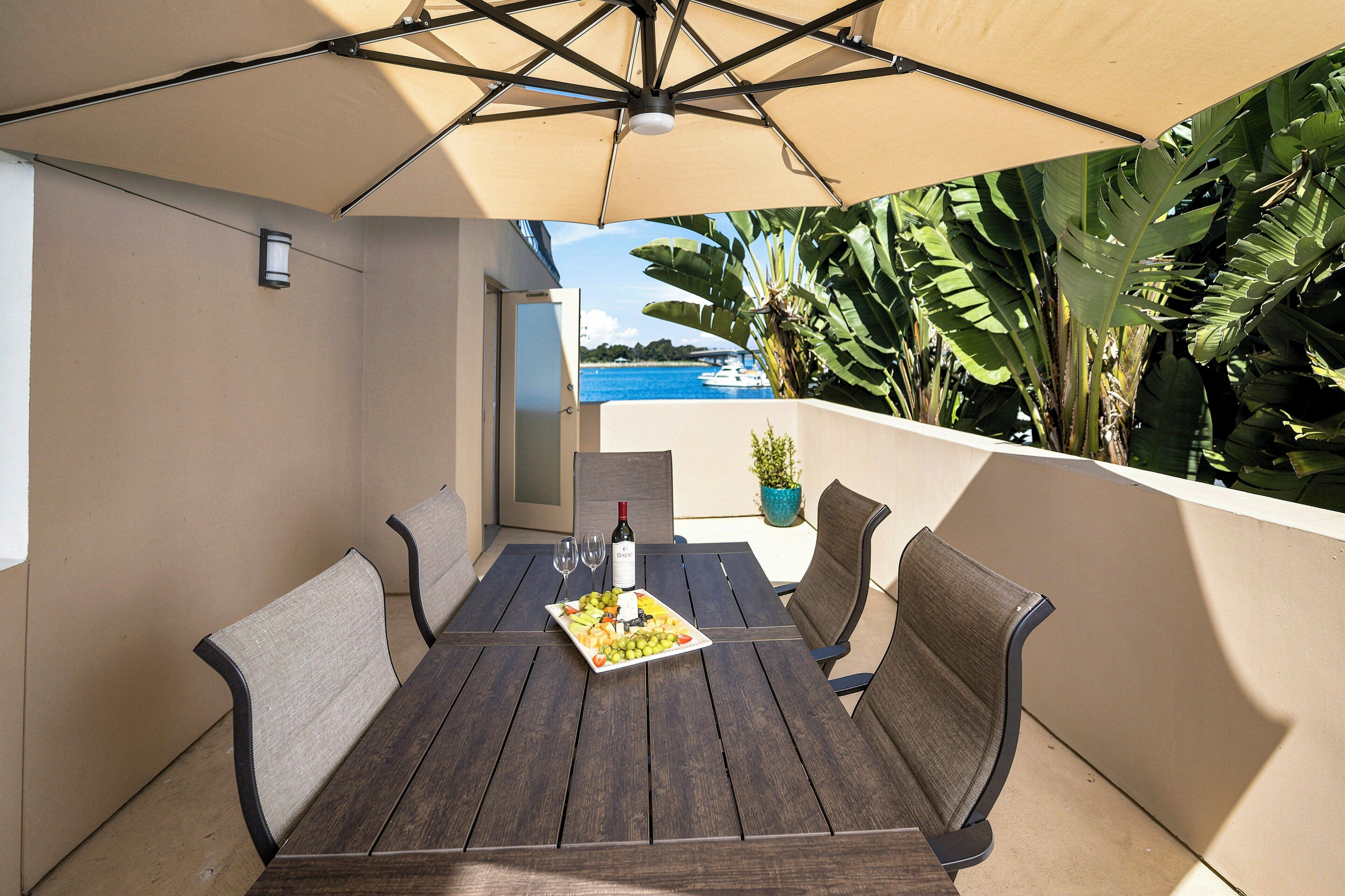 Un patio exterior con una mesa de madera, cuatro sillas, una botella de vino y una copa de vino.