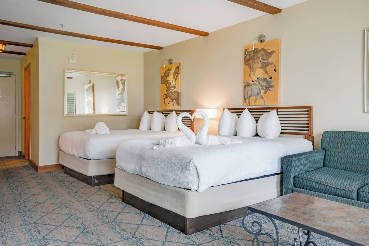 A hotel room with two beds, a sofa, a table, and artwork on the walls.