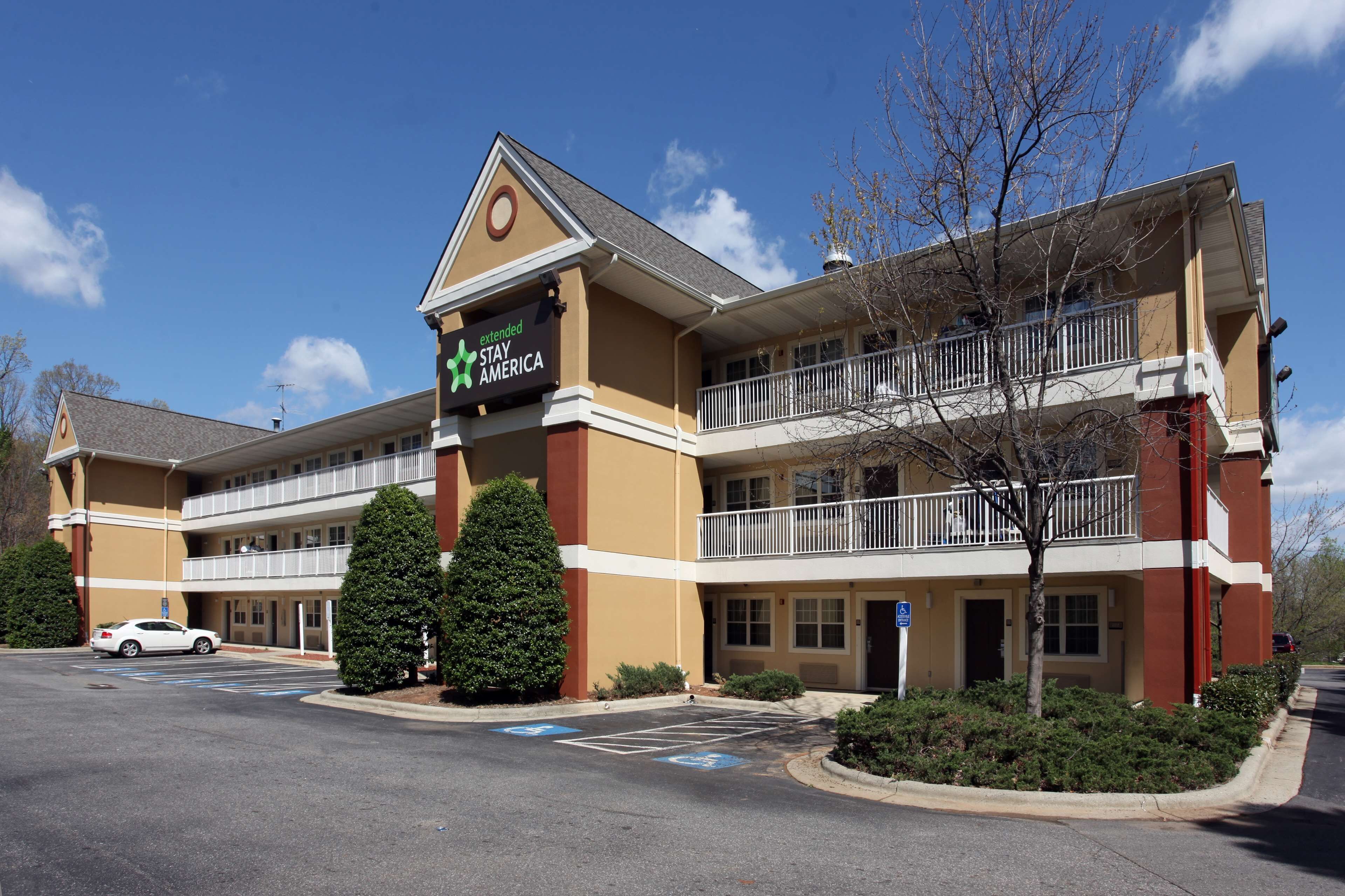 A Stay America hotel with a two-story structure, a parking lot, and a clear blue sky.