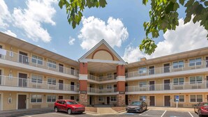A multi-story hotel with a central lobby, parking spaces, and a clear sky. - Extended Stay America Suites Greensboro Big Tree Way (Greensboro)