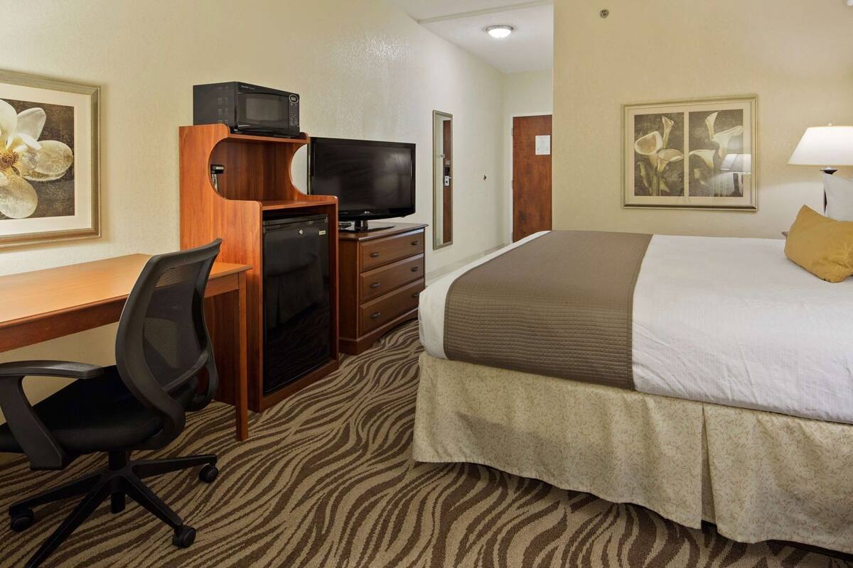 A hotel room with a bed, desk, chair, television, and artwork on the walls.