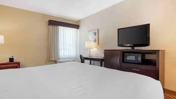 A hotel room with a large bed, a television, a desk with a lamp, and a microwave.