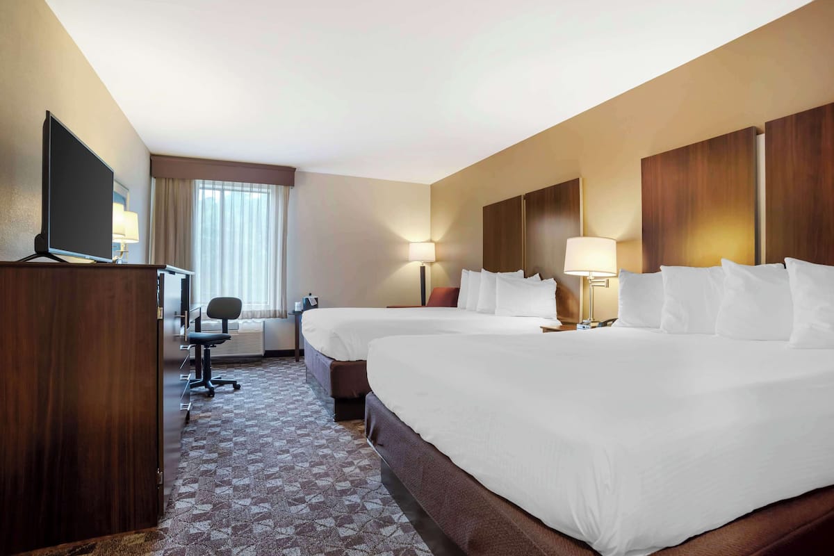 A hotel room with two beds, a desk, a TV, and a window with curtains.