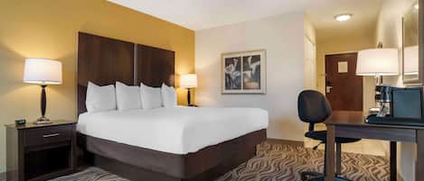 Quarto de hotel com uma cama grande, duas mesas de cabeceira com luminárias, uma escrivaninha com cadeira e um tapete estampado.