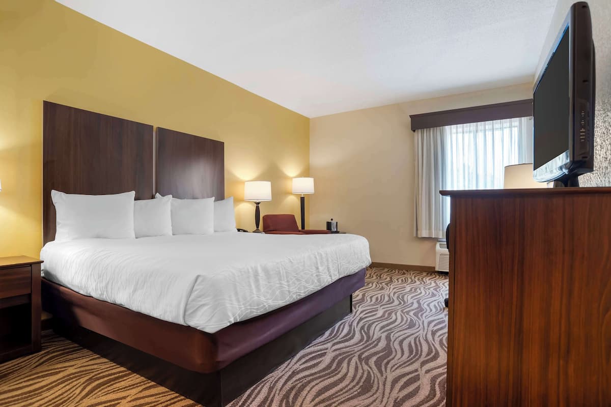 A hotel room with a large bed, two bedside lamps, a flat-screen TV, and a wooden desk.