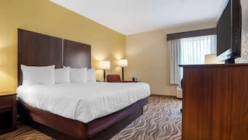 A hotel room with a large bed, two bedside lamps, a flat-screen TV, and a wooden desk.