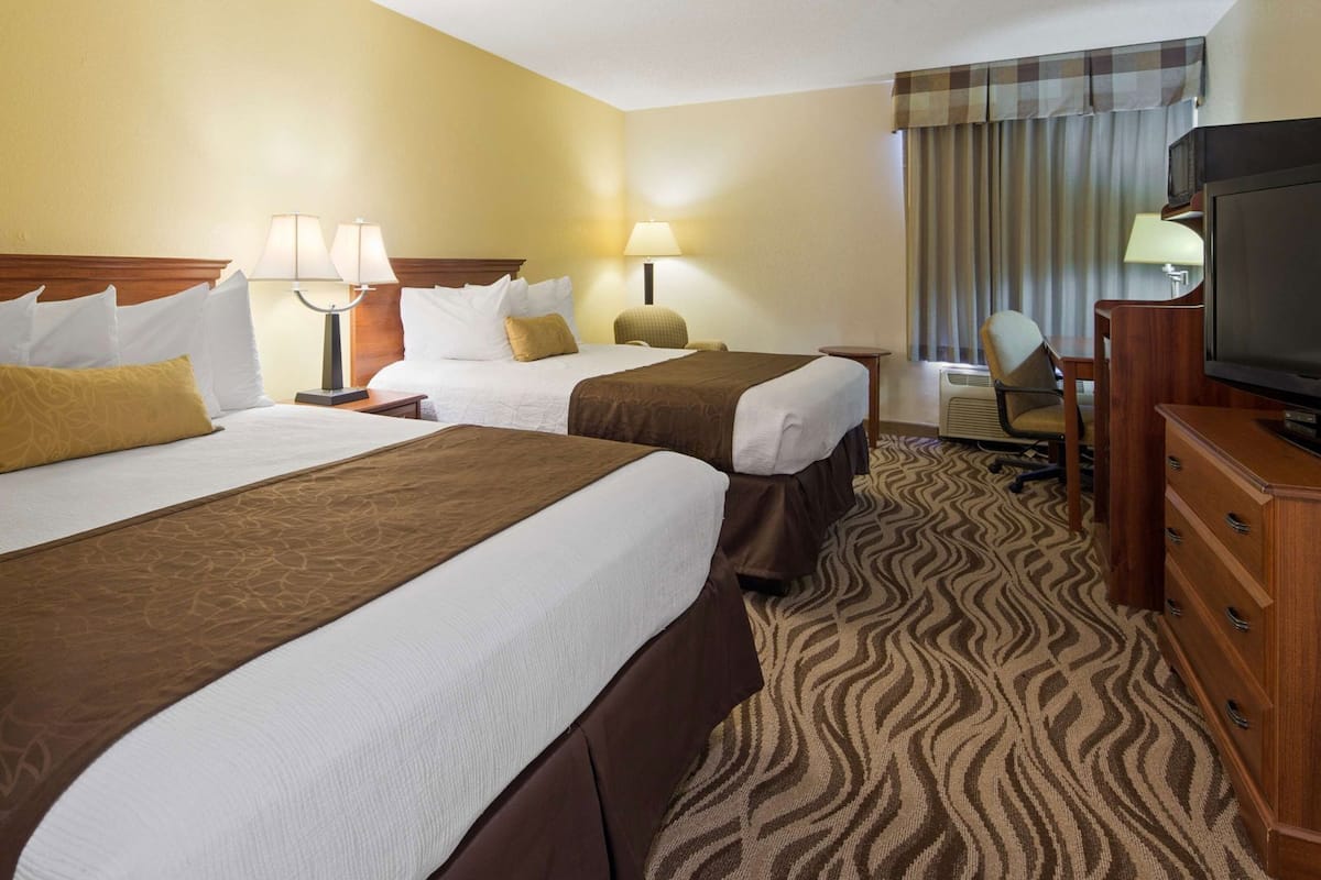 A hotel room with two beds, a television, a desk, and a chair.