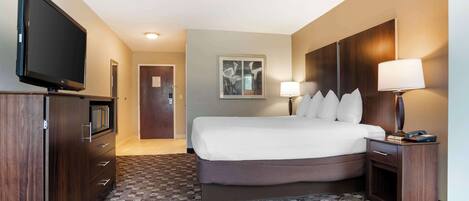 A hotel room with a large bed, a TV on a dresser, a desk with a lamp, and a framed picture on the wall.