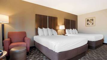 A hotel room with two beds, a red armchair, a small round table, and a trash bin.