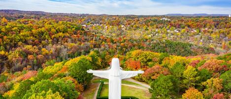 A large white statue with outstretched arms surrounded by a well-maintained garden and a forested area in the background.