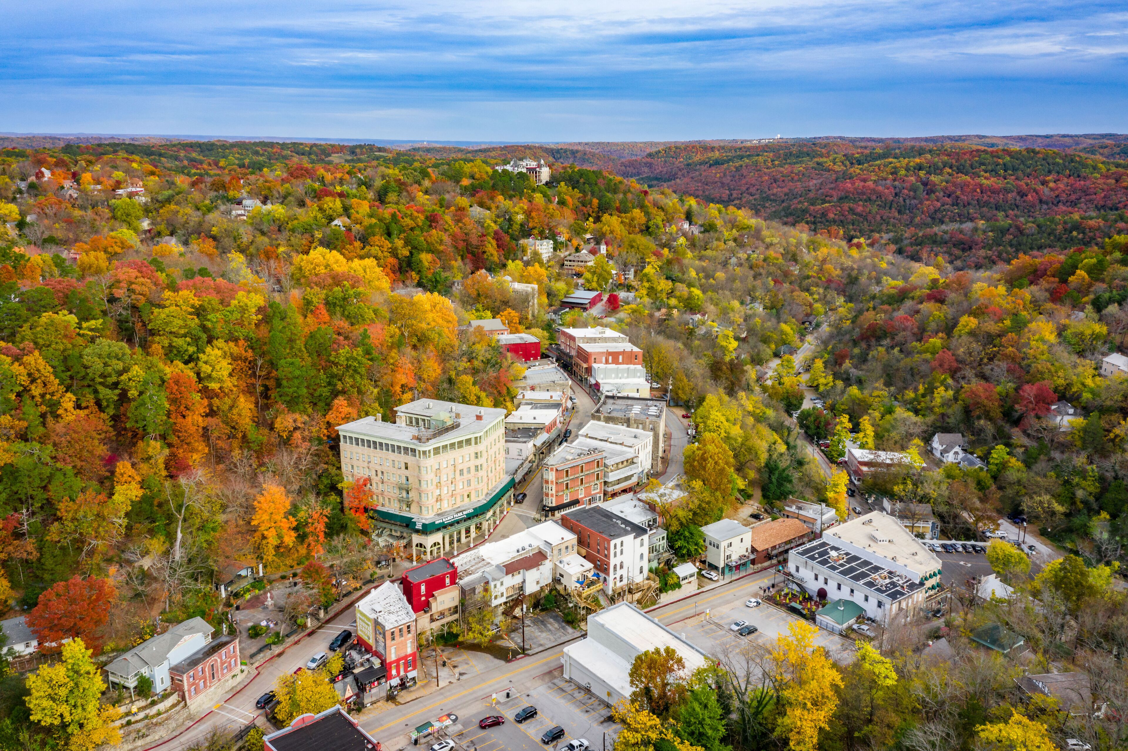 An aerial view of a town with a mix of residential and commercial buildings surrounded by autumn-colored trees.