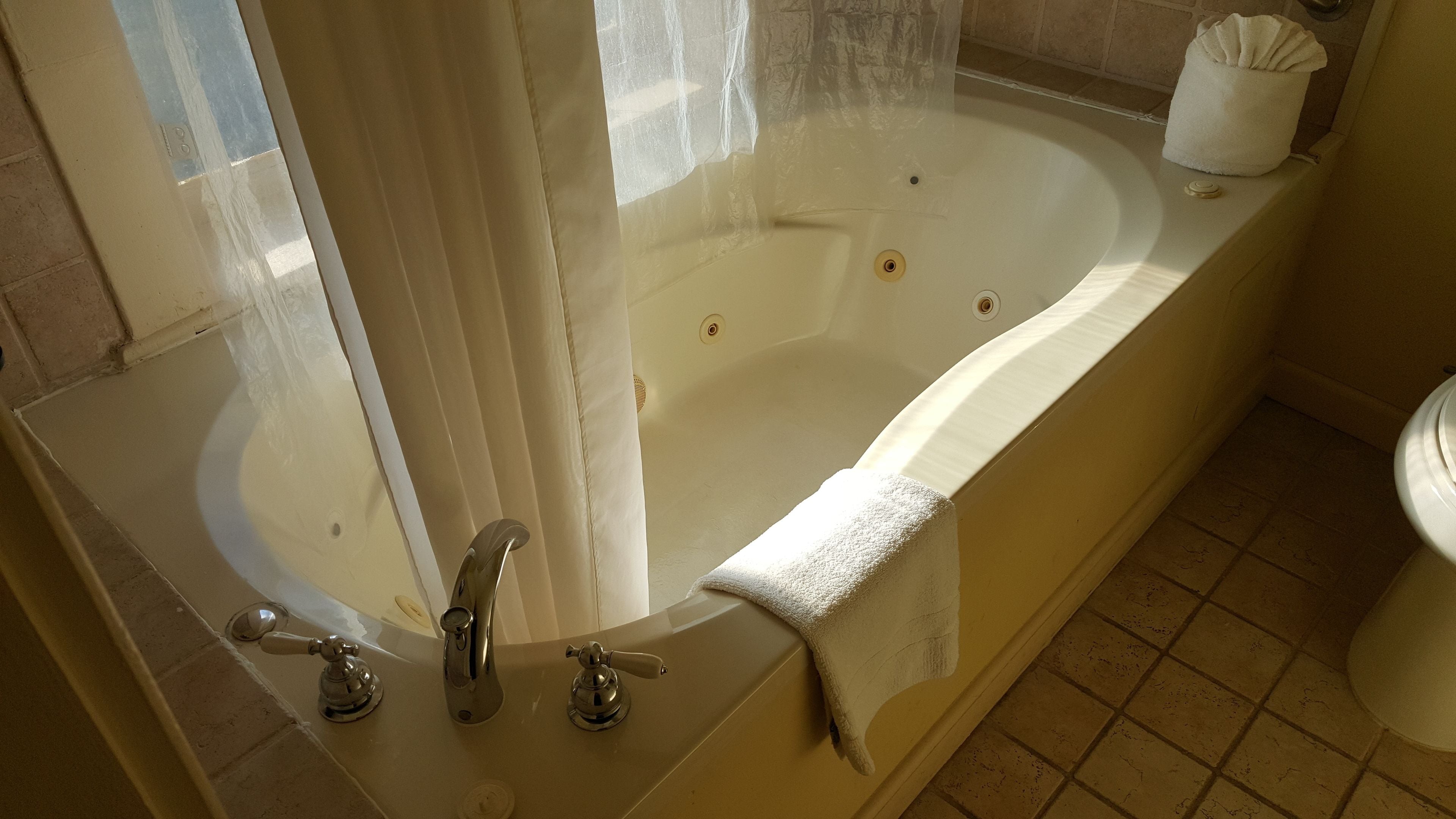A large freestanding bathtub with a shower curtain, a towel, and a toilet in a bathroom.