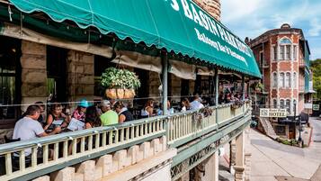 Un restaurante con terraza, toldo verde y un edificio de piedra al fondo.