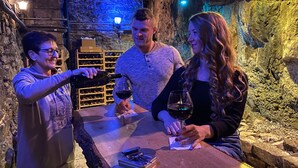 Three people toasting with wine glasses at a table in a cave-like setting with stone walls and dim lighting. - Basin Park Hotel and Spa (Eureka Springs)
