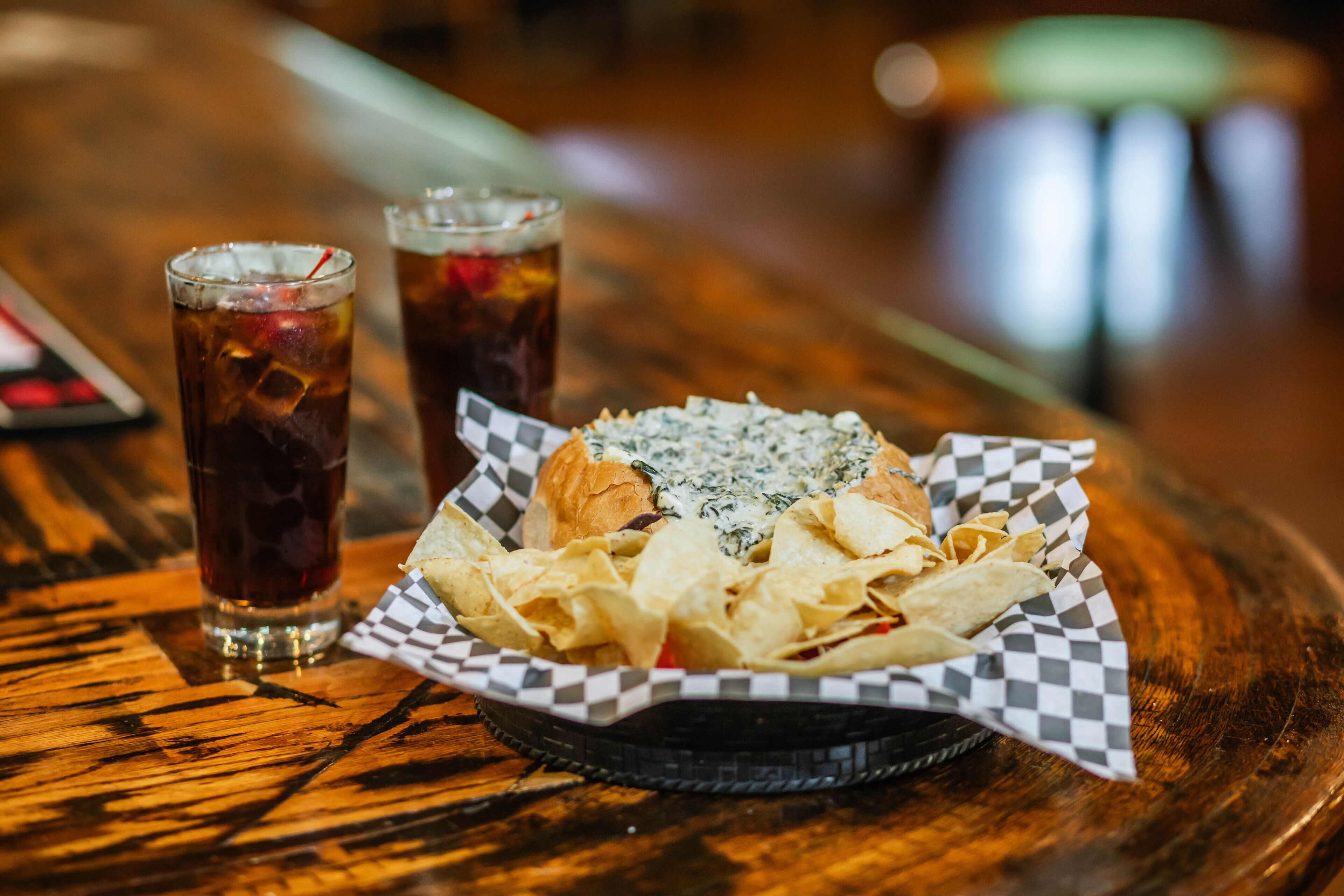 A meal consisting of nachos, a sandwich, and two iced drinks on a wooden table.