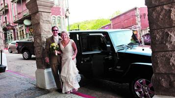 A wedding couple exiting a black SUV in front of a building with stone pillars and a red brick facade.