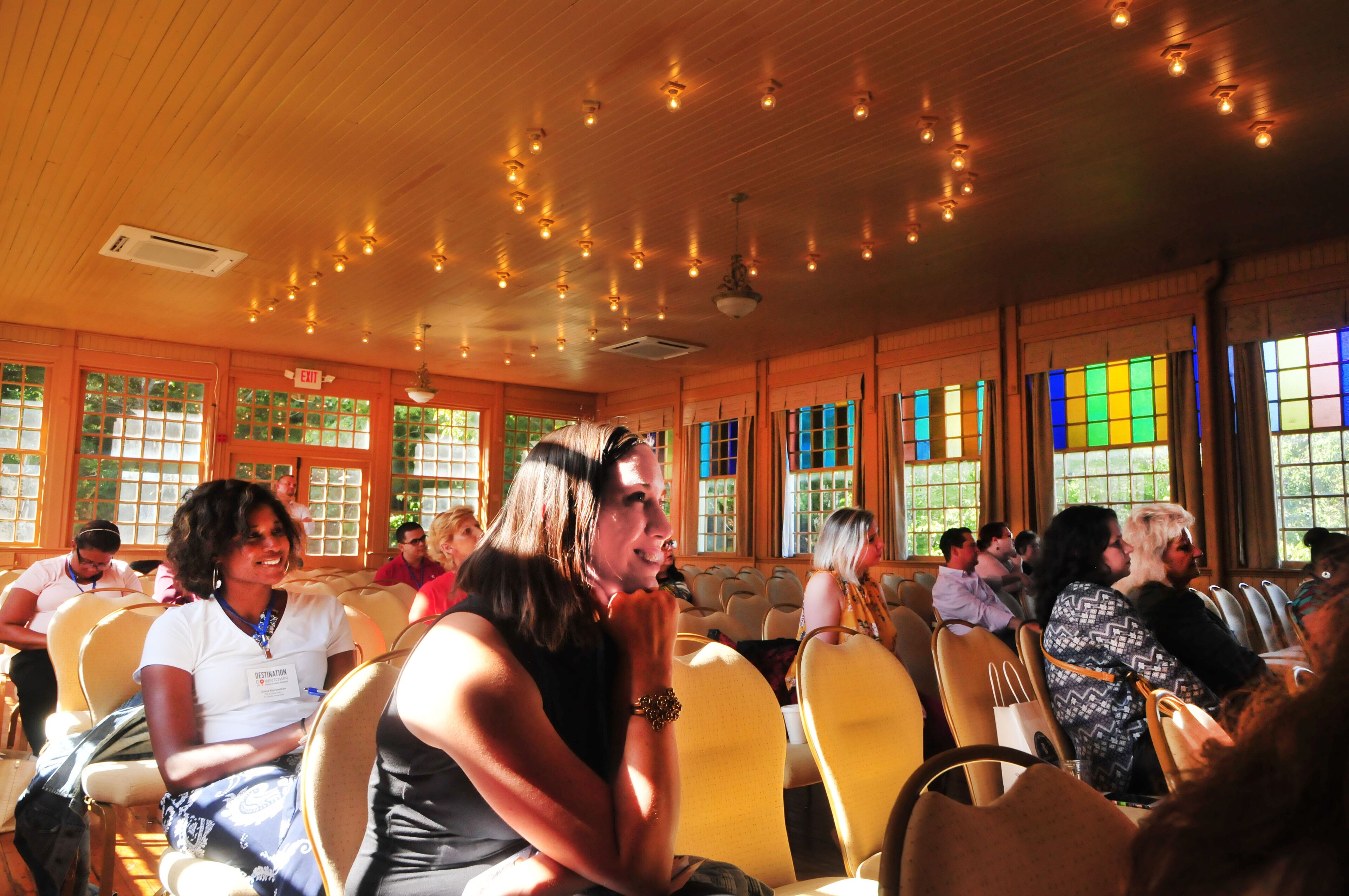 A conference room with rows of chairs, a wooden ceiling with hanging lights, and large windows with multiple panes.