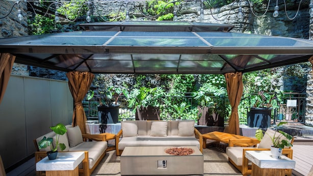 An outdoor seating area with a covered patio, cushioned sofas, wooden tables, and potted plants. - Basin Park Hotel and Spa (Eureka Springs)