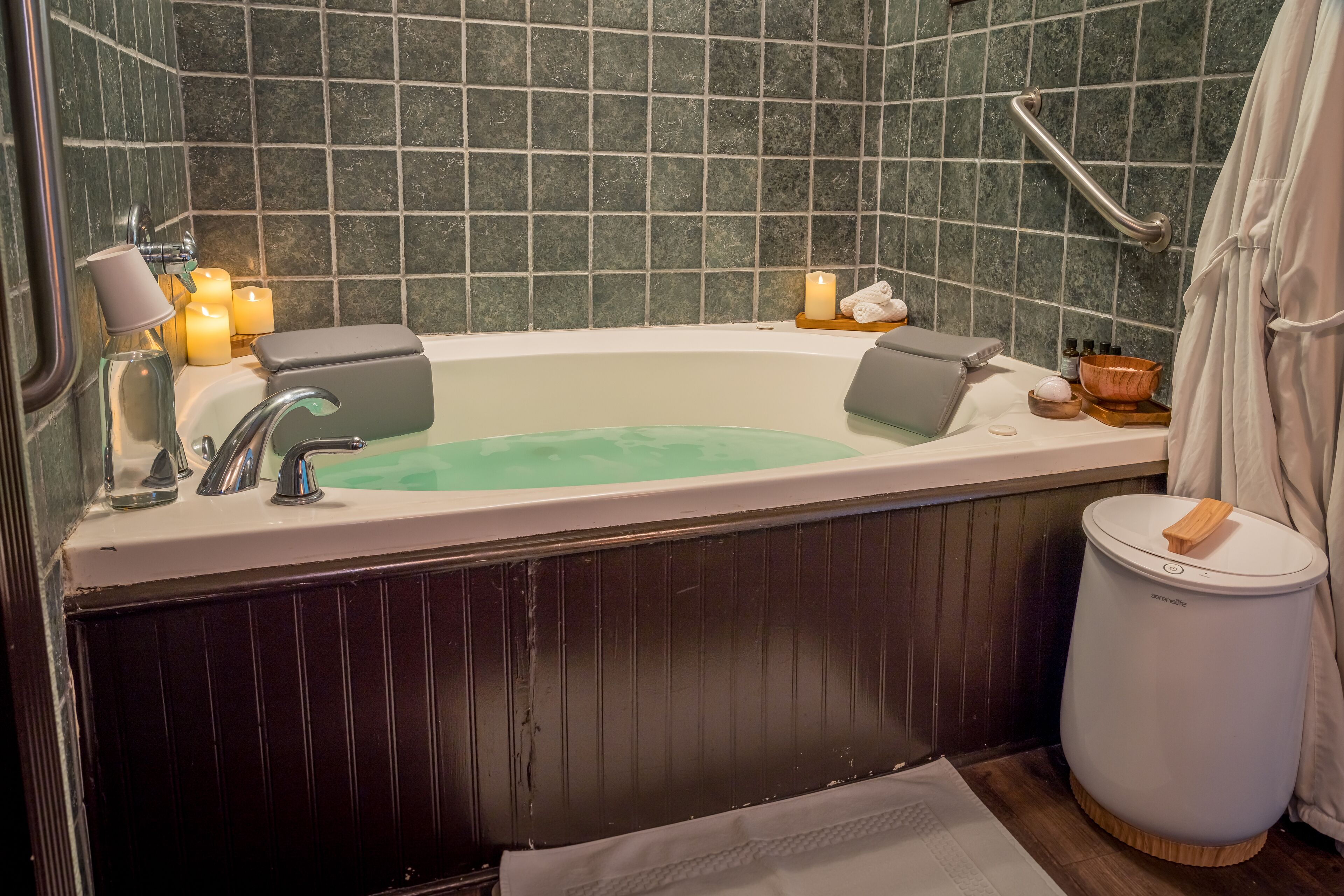 Un bagno con una vasca da bagno, un mancorrente, un cestino e delle candele.