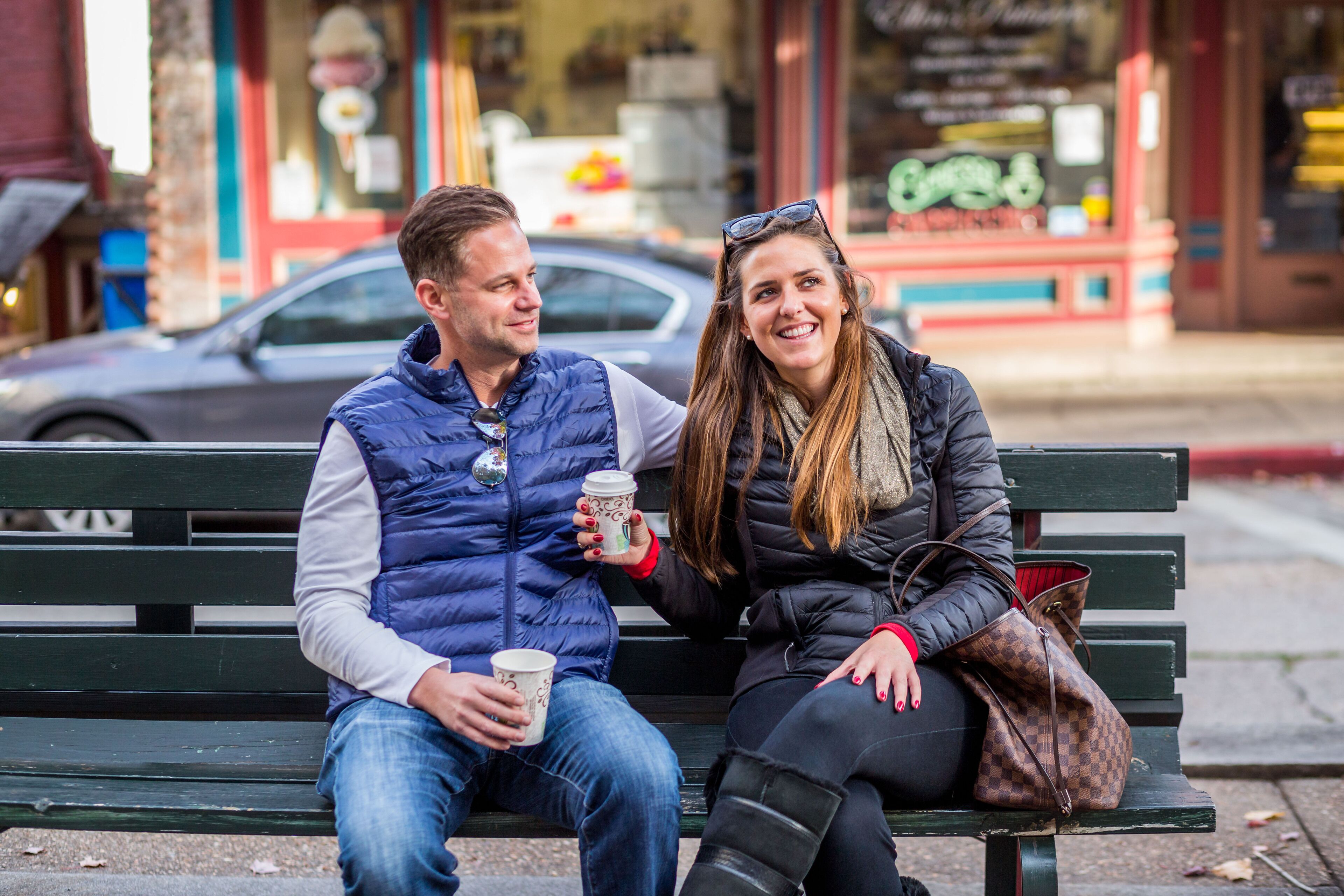 Two people sitting on a bench, holding coffee cups.