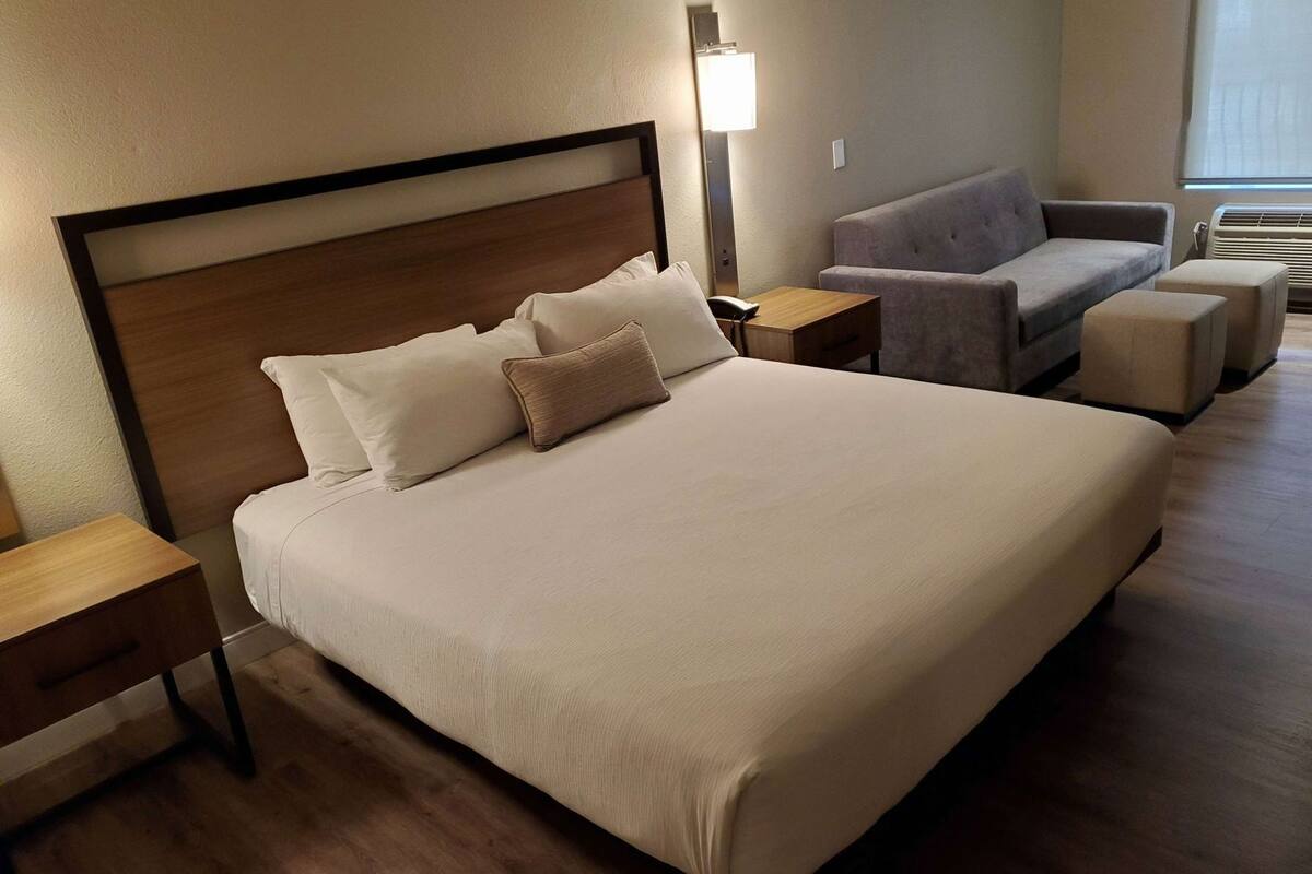 Una habitación de hotel con una cama grande, un sofá, una mesita y una lámpara.