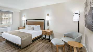 A hotel room with a large bed, bedside tables, a chair, a small table, and a wall-mounted lamp.