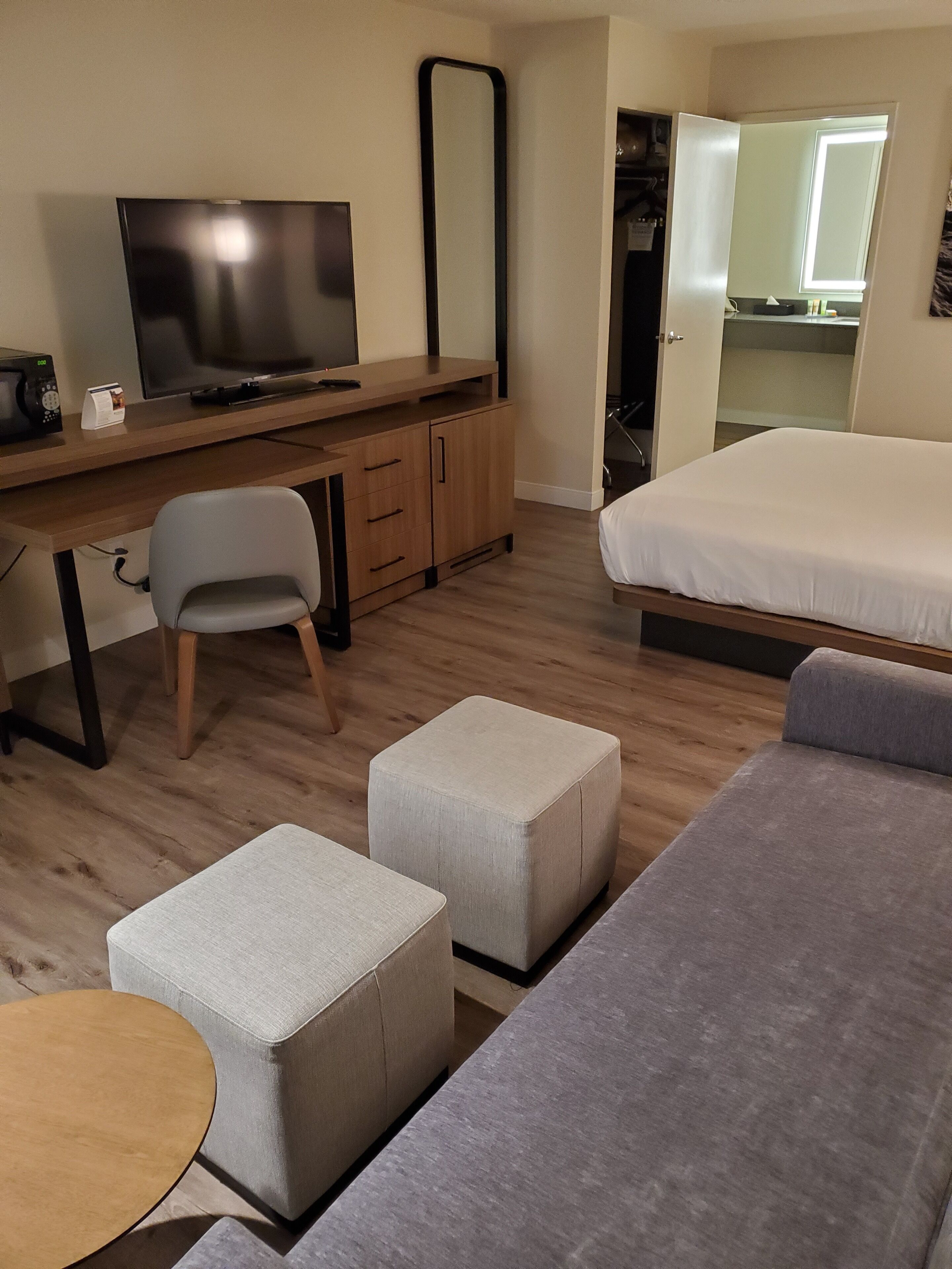 Een moderne hotelkamer met een houten bureau, een televisie, een grijze bank en een bed.