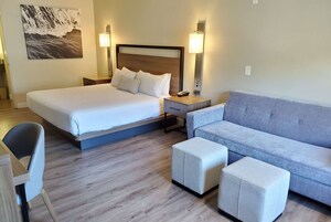Una habitación de hotel moderna con una cama grande, un sofá gris y una mesita.