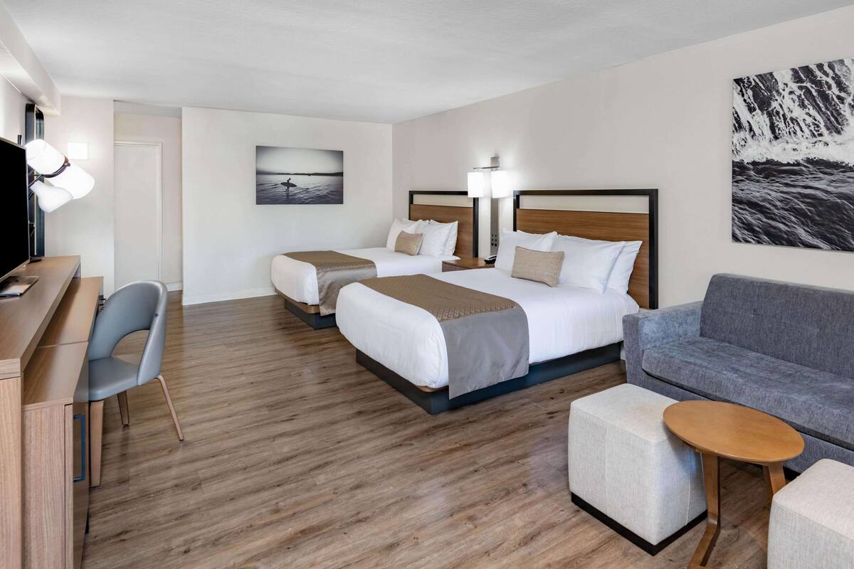 Una habitación de hotel con dos camas, un escritorio, una silla, un sofá y una pequeña mesa.