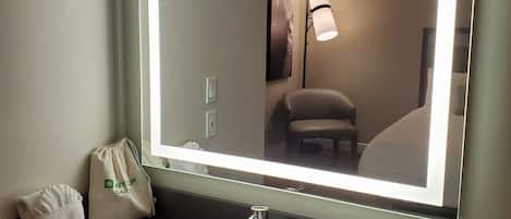 Un baño de hotel con un espejo grande, un lavamanos, una toalla y una pequeña bolsa con un logotipo.