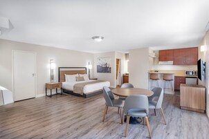 Habitación de hotel con cama, mesitas de noche, escritorio, mesa de comedor con sillas, zona de cocina y televisor.