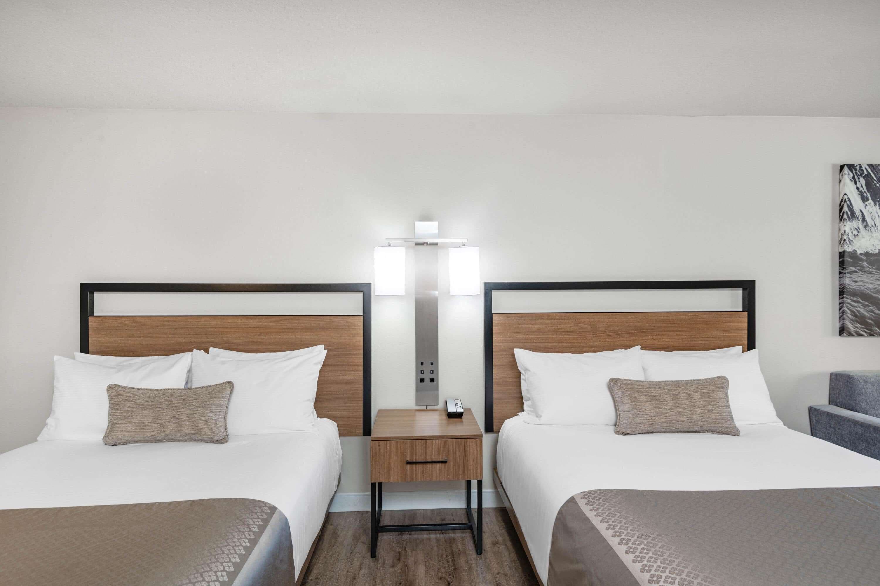 A hotel room with two beds, a nightstand with a lamp, and a painting on the wall.