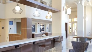 Eine moderne Hotelhalle mit einer Rezeption, einer Bar und Sitzgelegenheiten mit Barhocker und gepolsterten Sesseln.