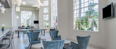 En moderne hotellobby med et stort spiseområde, siddepladser og store vinduer med udsigt over omgivelserne.