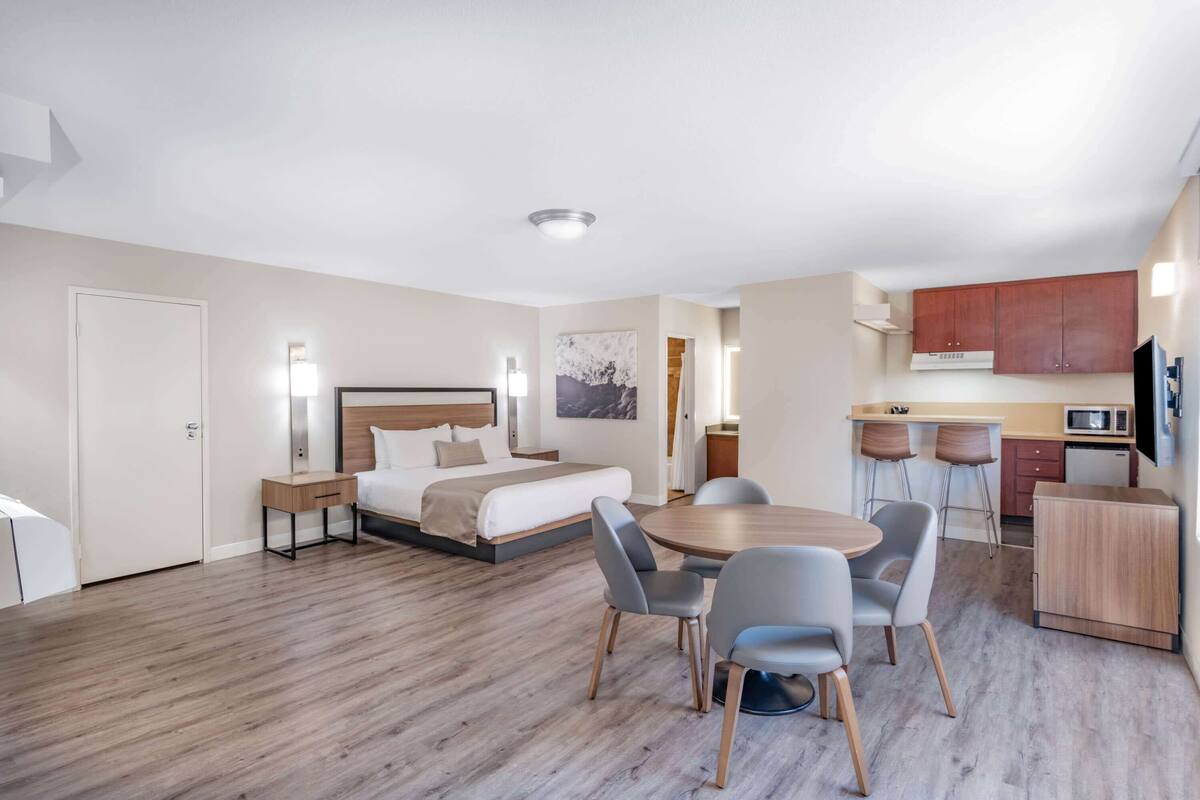Una habitación de hotel moderna con una cama, mesita de noche y un área de comedor con sillas y una mesa.