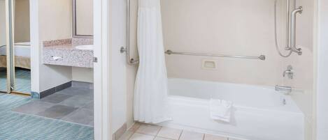 A bathroom with a bathtub, grab bars, a towel, and a sink with a mirror.