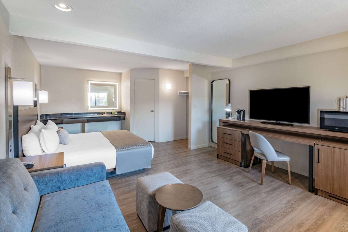 Una habitación de hotel moderna con una cama, un escritorio, un televisor y un espacio para sentarse.