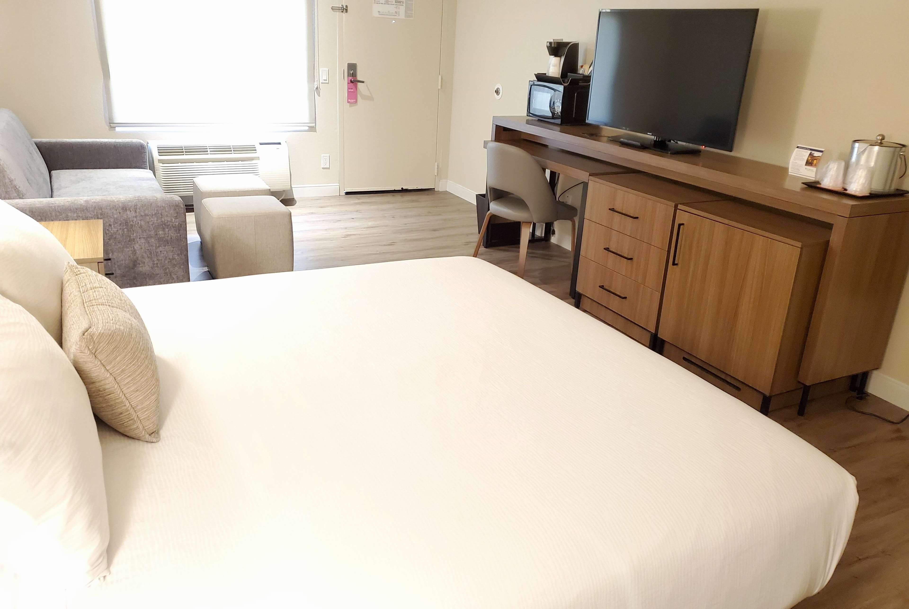 A hotel room with a large bed, a desk with a TV, a chair, and a wardrobe.