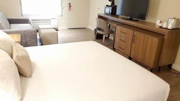 A hotel room with a large bed, a desk with a TV, a chair, and a wardrobe.