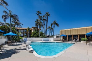 A swimming pool with lounge chairs and umbrellas, surrounded by palm trees and a building with balconies. - Wyndham Garden San Diego Near SeaWorld (San Diego)