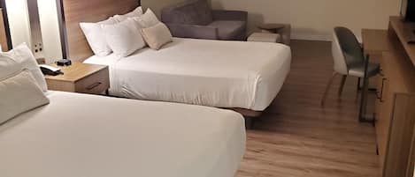Una habitación de hotel con dos camas, un escritorio, una silla, un sofá y una lámpara.