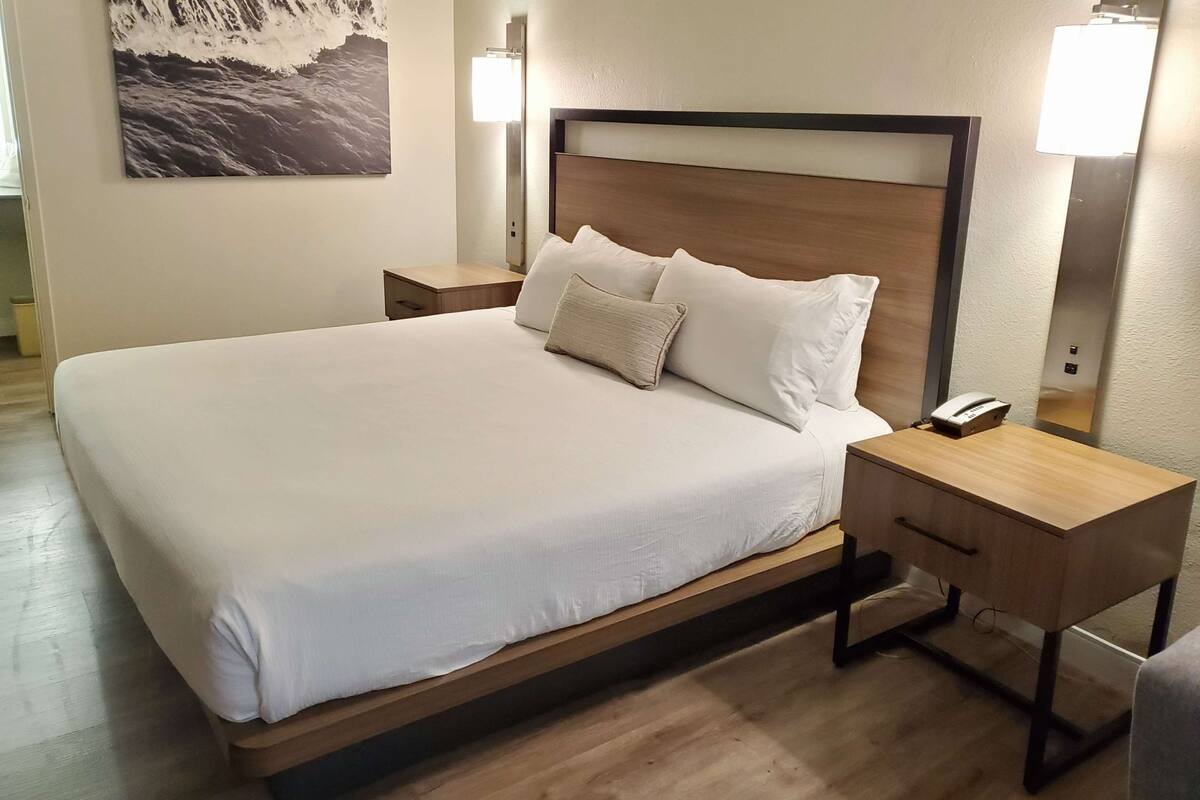 Una cama bien hecha con cabecera de madera, dos mesitas de noche con lámparas y un teléfono fijado a la pared.