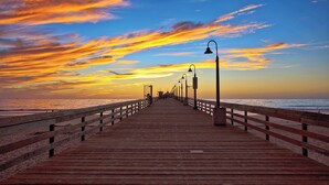 Un muelle de madera que se adentra en el océano, con un atardecer de fondo.