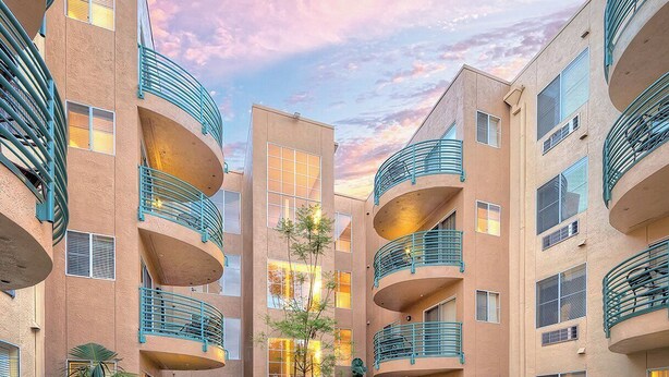 Un edificio de varios pisos con balcones, un patio central con una fuente y mesas al aire libre.