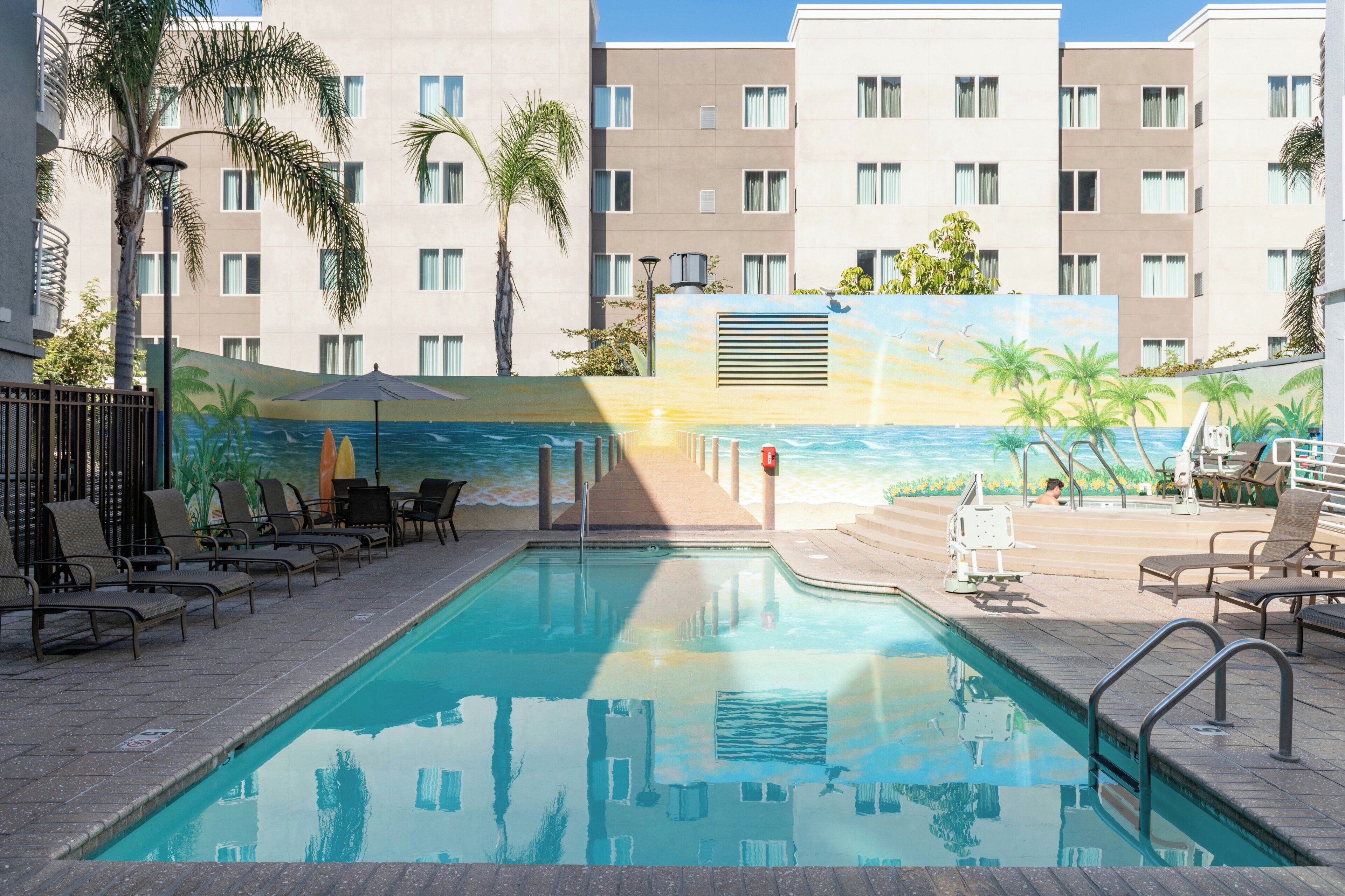Ein Schwimmbecken mit Liegestühlen, Palmen und einer Wandmalerei mit Strandmotiv.