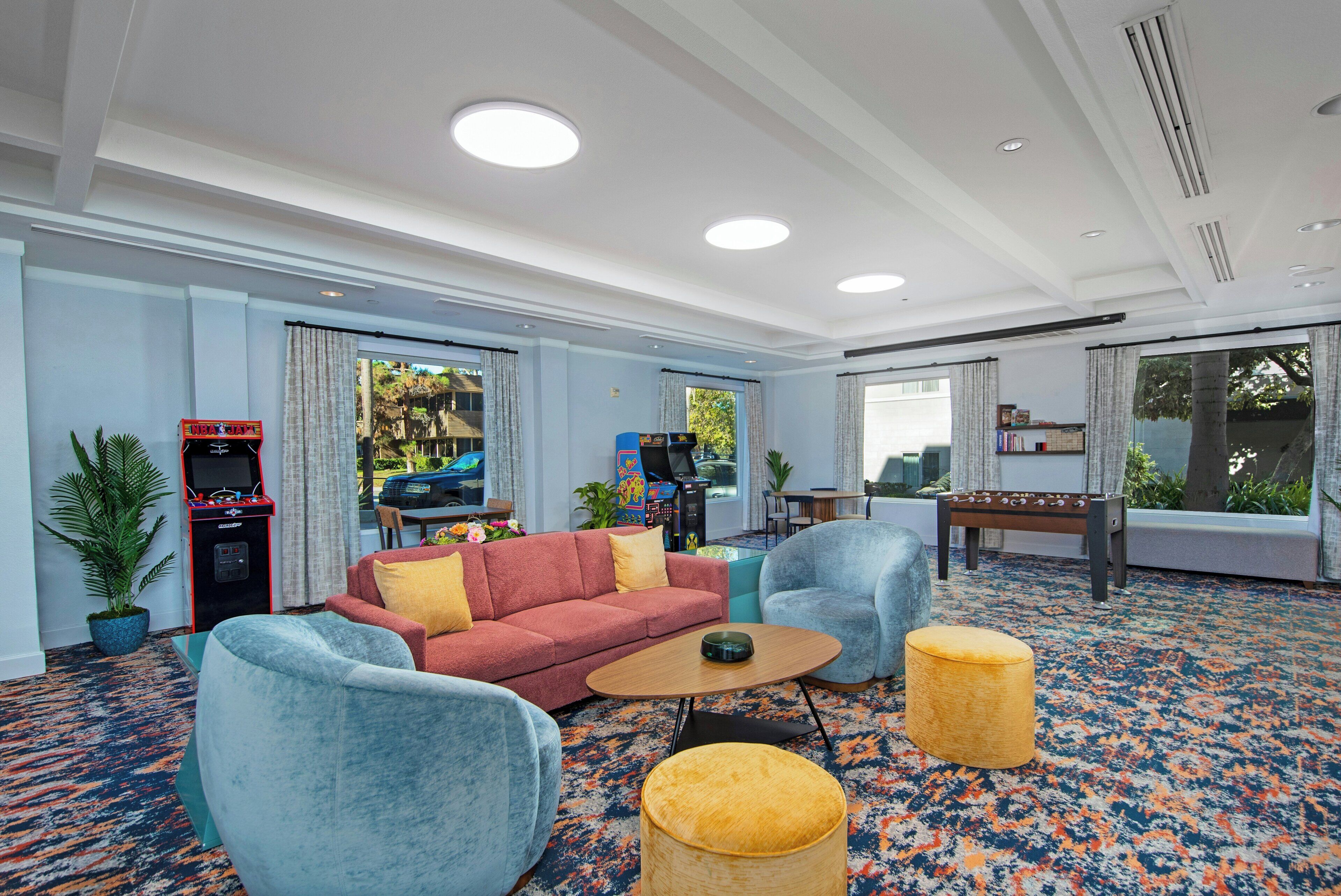 Un hall d’hôtel avec un canapé rouge, des fauteuils bleus, une table basse, une table de baby-foot et un sol recouvert de moquette.