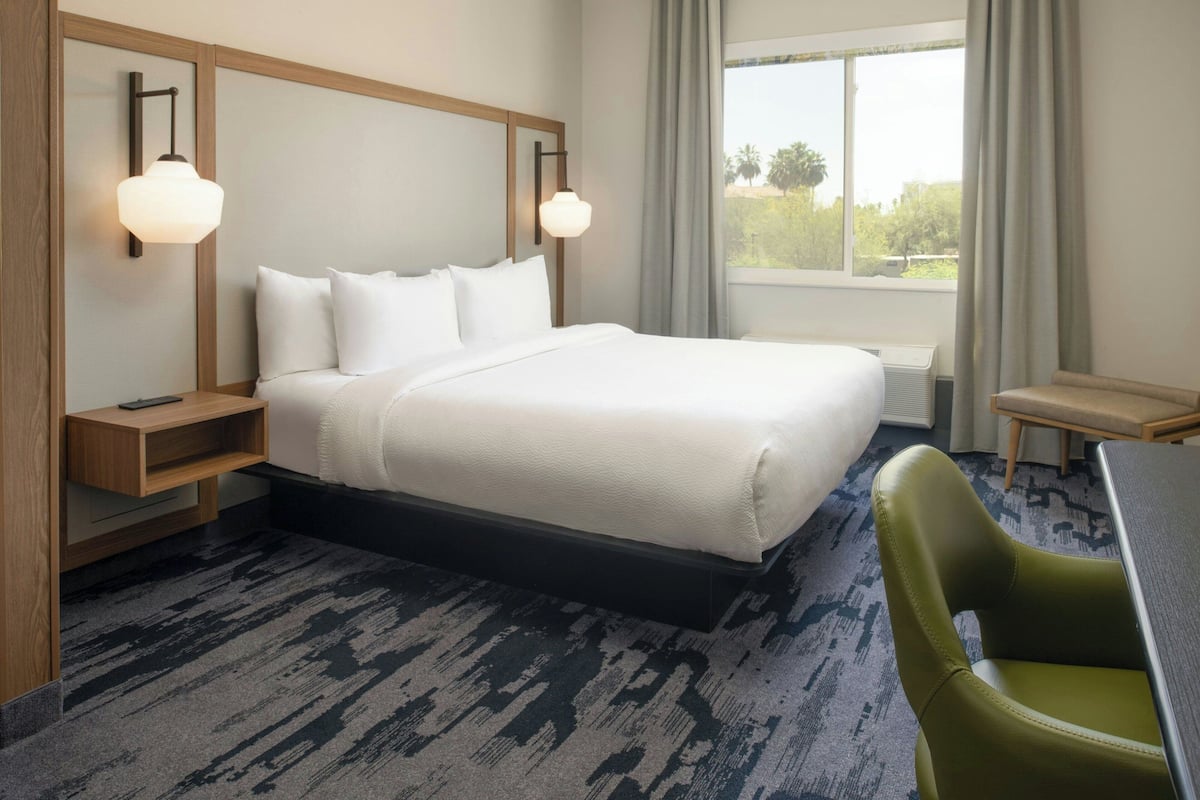 A hotel room with a large bed, bedside tables, a desk, a chair, and a window with curtains.