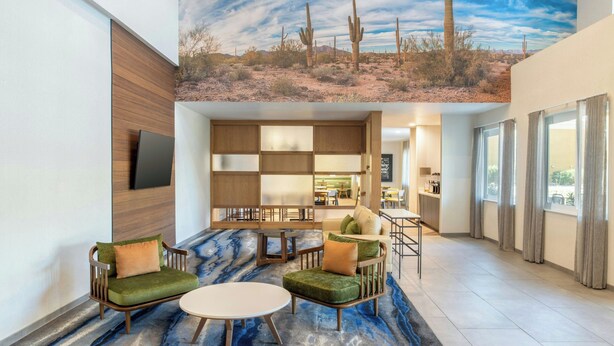 A lobby with a desert mural, a seating area with green upholstered chairs, and a kitchen visible in the background. - Fairfield Inn & Suites by Marriott Scottsdale Old Town (Scottsdale)