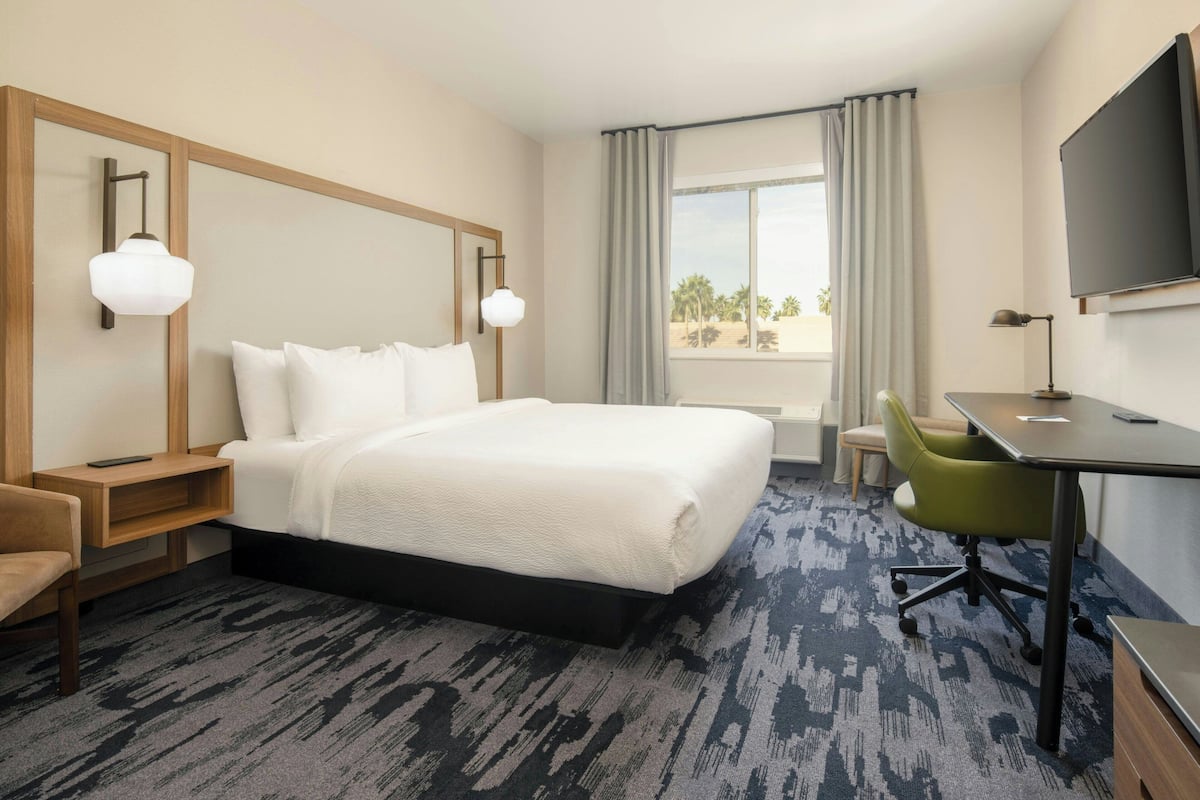 A hotel room with a large bed, a desk, a chair, a TV, and a window with curtains.