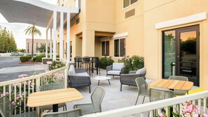 An outdoor patio with seating arrangements, including tables and chairs, and a building entrance with a glass door. - Fairfield Inn & Suites by Marriott Scottsdale Old Town (Scottsdale)